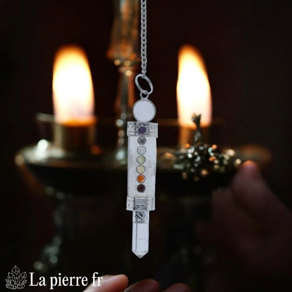 Main tenant un pendule en cristal de roche et 7 chakras au-dessus d'une carte, pour une séance de guidance intuitive