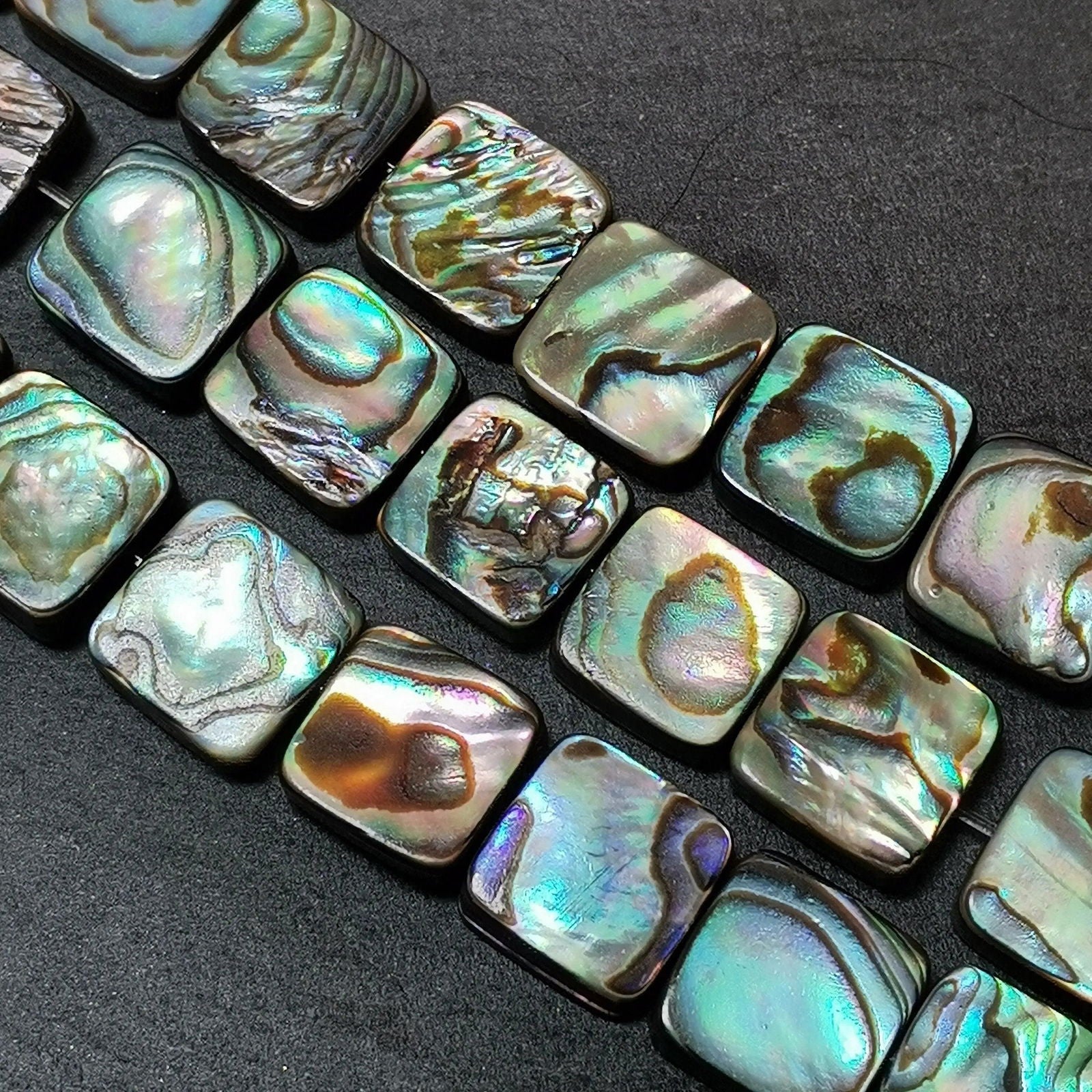 Gros plan sur des perles carrées de nacre abalone, reflets bleu-vert nacrés pour collier et bracelet