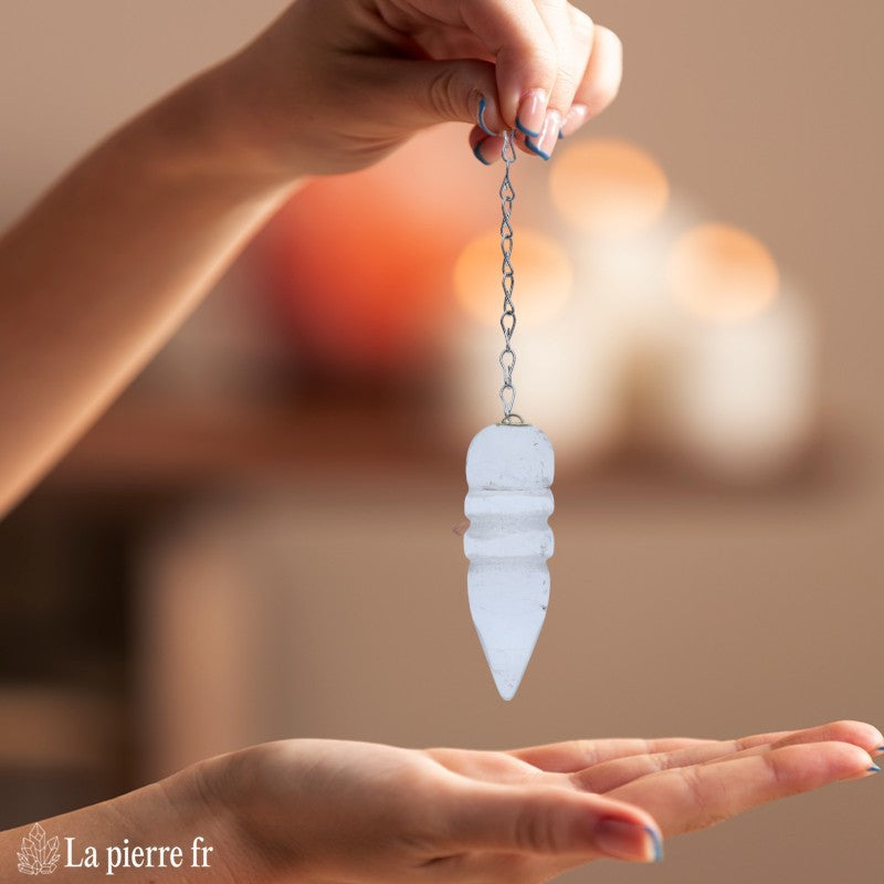 Pendule égyptien en cristal de roche oscillant au-dessus d'une planche de radiesthésie Fleur de Vie