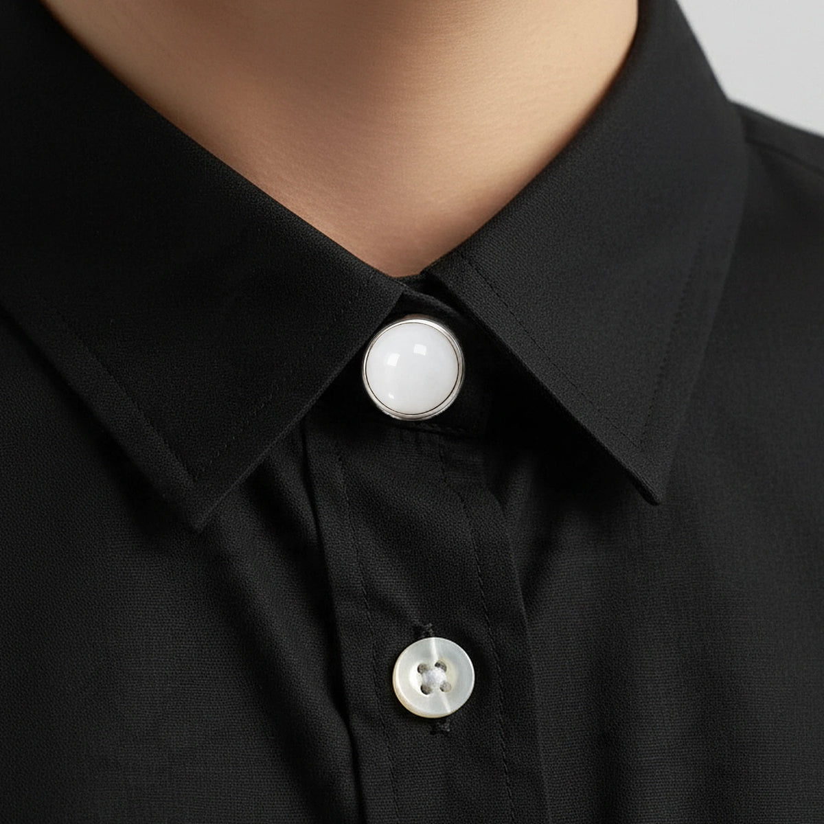 Cache bouton en jade blanc clipsé au col d'une chemise noire