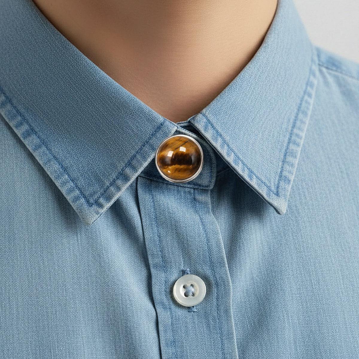 Bijou de chemise en œil de tigre clipsé sur le bouton du col d'une chemise en jean bleu clair