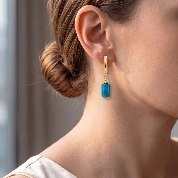 Créole dorée avec tube d'apatite bleue portée à l'oreille d'une femme, un bleu intense