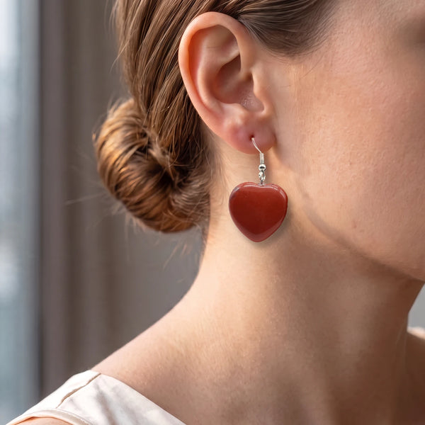 Boucles d'oreilles cœur en jaspe rouge portées à l'oreille d'une femme, pendantes sur crochet argenté