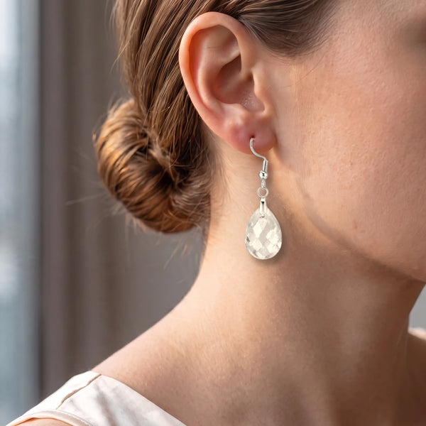 Boucle d'oreille cristal de roche portée par une femme, goutte facettée claire et lumineuse