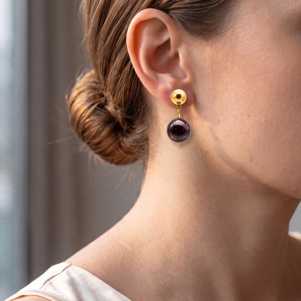 Puce dorée avec boule de grenat rouge profond portée à l'oreille d'une femme, style élégant