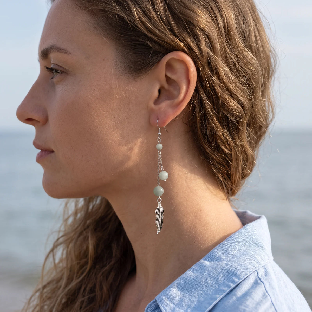Boucle d'oreille pendante en aigue-marine avec plume argentée, portée à l'oreille