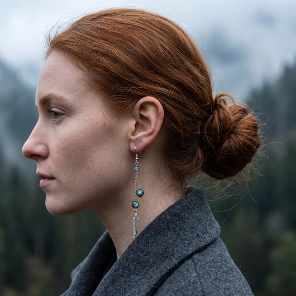 Boucle d'oreille pendante en labradorite avec plume argentée, portée à l'oreille