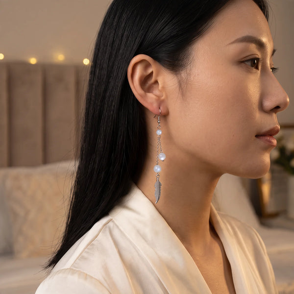 Boucle d'oreille pendante en pierre de lune avec plume argentée, portée à l'oreille