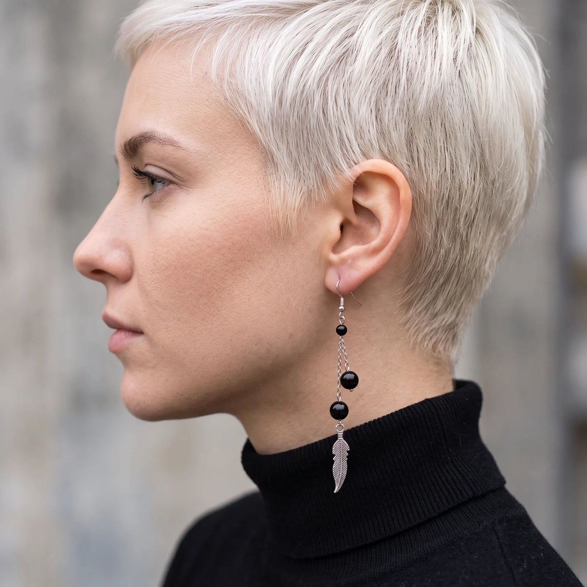 Boucle d'oreille pendante en tourmaline noire avec plume argentée, portée à l'oreille
