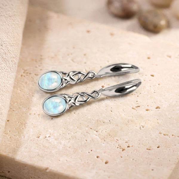 Boucles d'oreilles en pierre de lune ovale à motif celtique en argent 925, paire posée sur une dalle de travertin