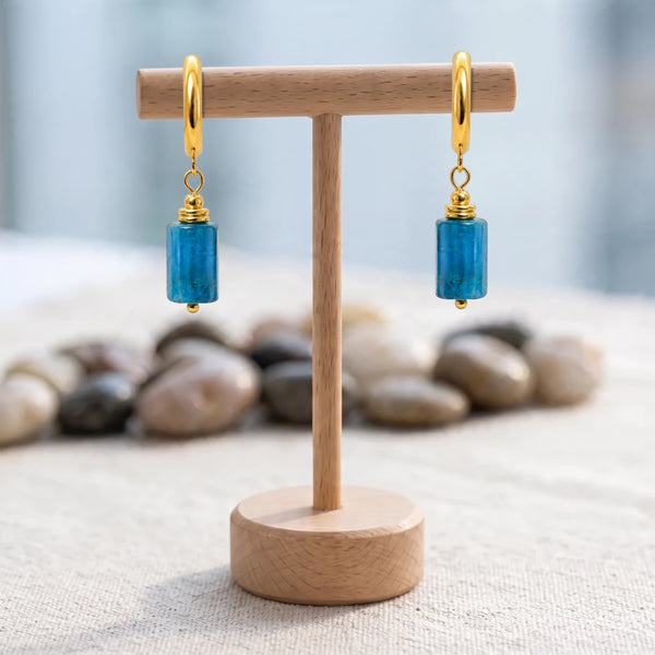 Boucles d'oreilles pendantes pierre bleue, tube d'apatite sur créole dorée, sur un support en bois