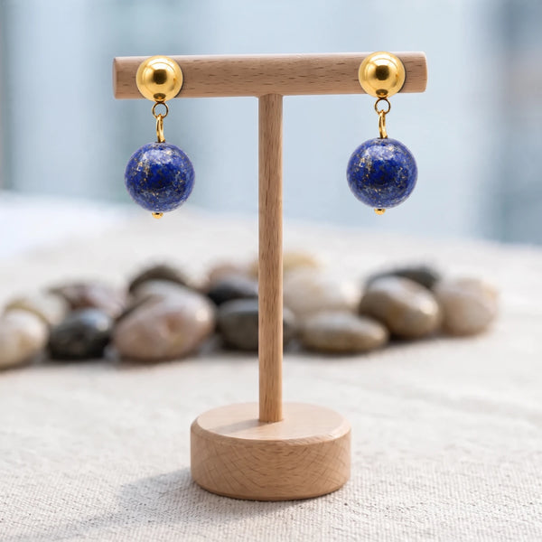 Boucles d'oreilles pierre bleue, boule de lapis-lazuli 12 mm sur puce dorée, présentées sur un support en bois