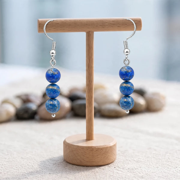 Boucles d'oreilles pierre bleue, trois boules de lapis-lazuli sur crochet acier argenté, sur un support en bois
