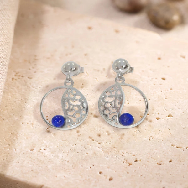 Boucles d'oreilles en lapis-lazuli sur cercle ajouré en argent 925 rhodié, paire posée à plat sur une dalle de travertin