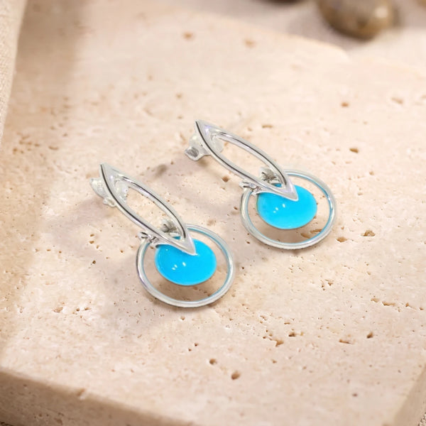 Boucles d'oreilles boule de turquoise dans un cercle en argent 925 rhodié, paire posée sur une dalle de travertin