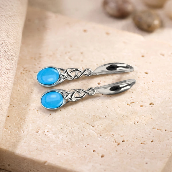 Boucles d'oreilles en turquoise ovale à motif celtique en argent 925, paire posée sur une dalle de travertin
