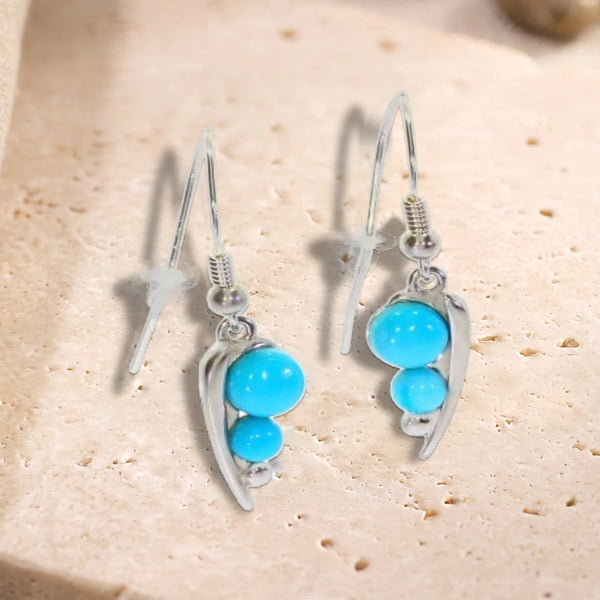 Boucles d'oreilles crochet en argent 925 rhodié, feuille et deux perles de turquoise, posées à plat sur du travertin
