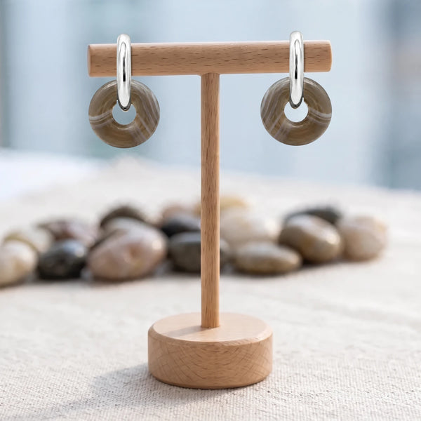 Boucles d'oreilles pierre grise, donut d'agate du Botswana 15 mm sur créole argentée, présentées sur un support en bois