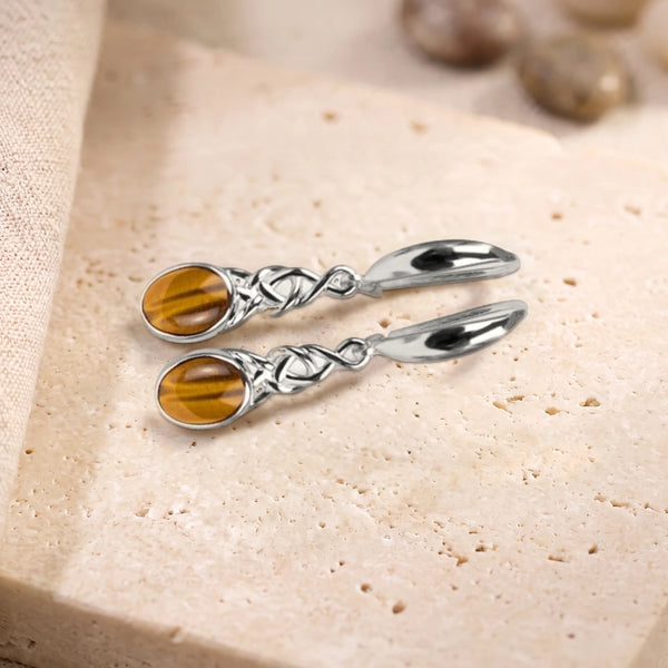 Boucles d'oreilles en œil de tigre ovale à motif celtique en argent 925, paire posée sur une dalle de travertin