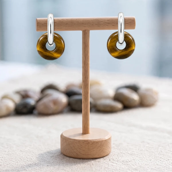 Boucles d'oreilles pierre marron dorée, donut d'œil de tigre 15 mm sur créole acier argenté, sur un support en bois