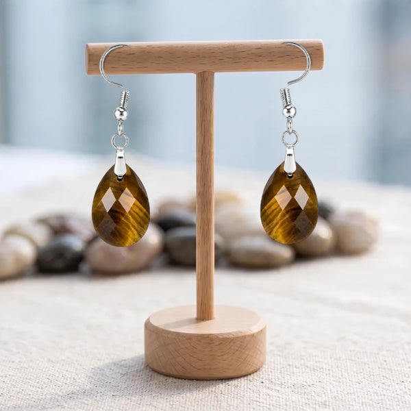 Boucles d'oreilles pierre marron dorée, goutte d'œil de tigre facettée sur crochet argenté, sur un support en bois