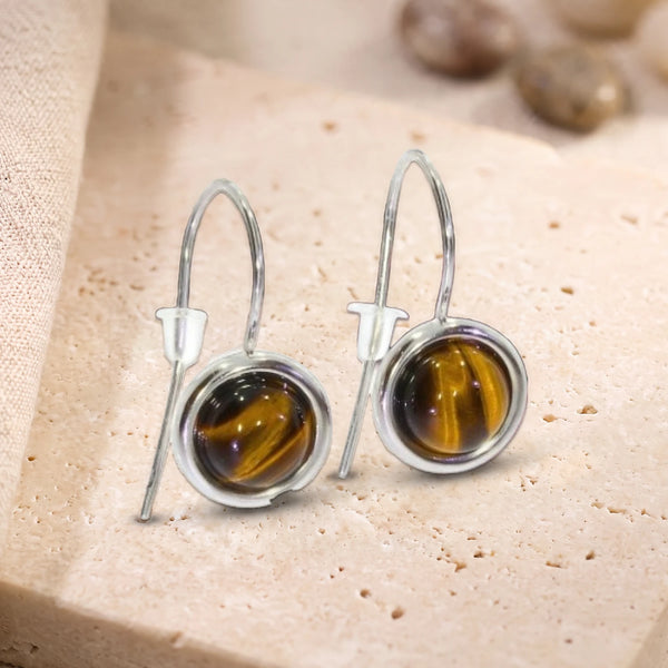 Boucles d'oreilles pendantes en œil de tigre, pierre ronde sertie sur crochet en argent 925 rhodié, posées sur travertin
