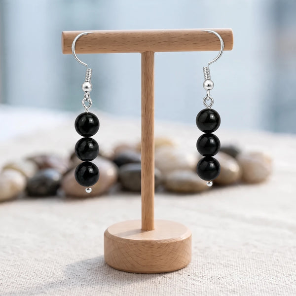 Boucles d'oreilles pierre noire, trois boules d'obsidienne sur crochet acier argenté, présentées sur un support en bois