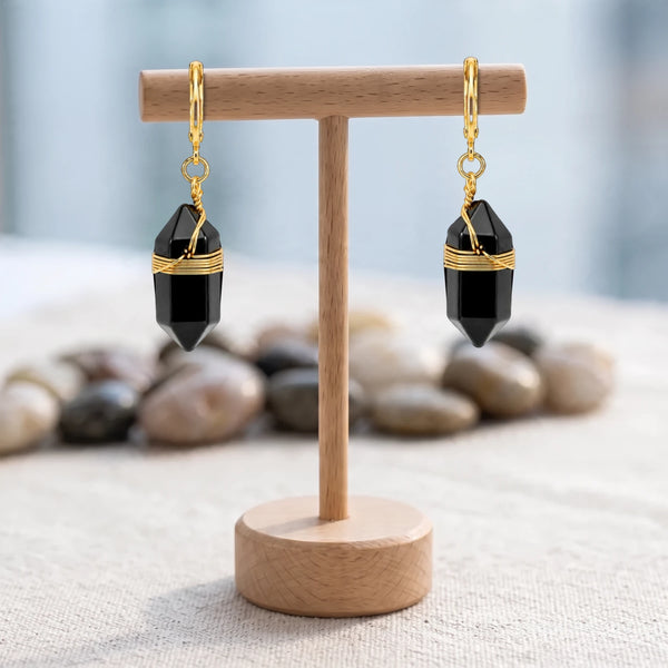 Boucles d'oreilles noir et doré, pointe d'obsidienne noire sur créole, suspendues à un présentoir en bois