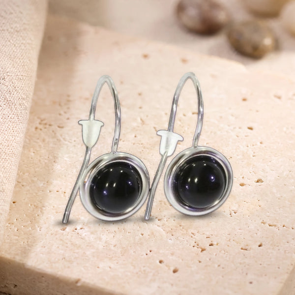 Boucles d'oreilles pendantes en onyx noir, pierre ronde sertie sur crochet en argent 925 rhodié, posées sur du travertin