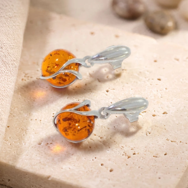 Boucles d'oreilles boule d'ambre en argent 925 rhodié, paire posée sur une dalle de travertin