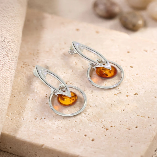 Boucles d'oreilles boule d'ambre dans un cercle en argent 925 rhodié, paire posée sur une dalle de travertin