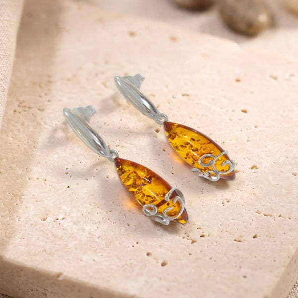 Boucles d'oreilles en ambre cabochon navette sur argent 925 rhodié, paire posée sur une dalle de travertin
