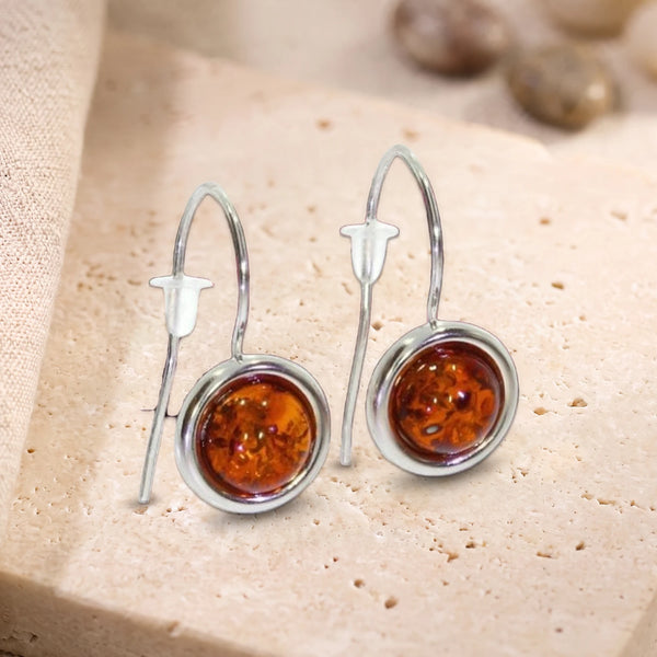 Boucles d'oreilles pendantes en ambre cognac, pierre ronde sertie sur crochet en argent 925 rhodié, sur travertin