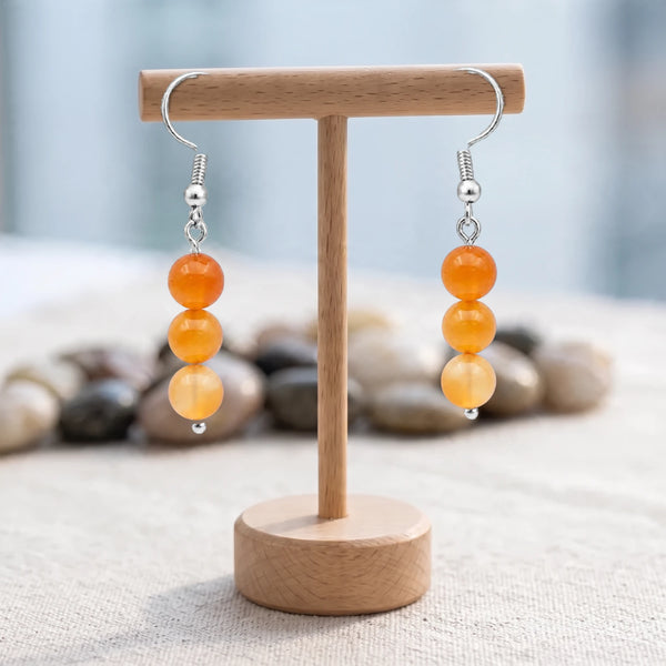Boucles d'oreilles pierre orange, trois boules de cornaline de 6 mm sur crochet argenté, sur un support en bois