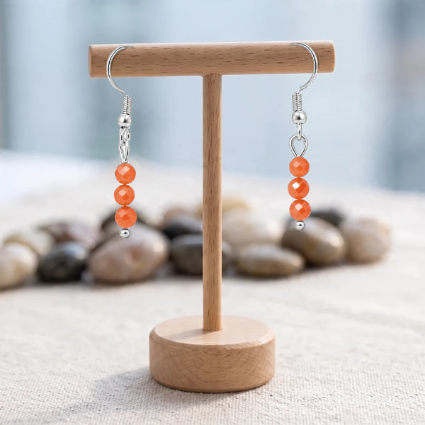 Boucles d'oreilles pierre orange, trois perles facettées de cornaline sur crochet acier argenté, sur un support en bois