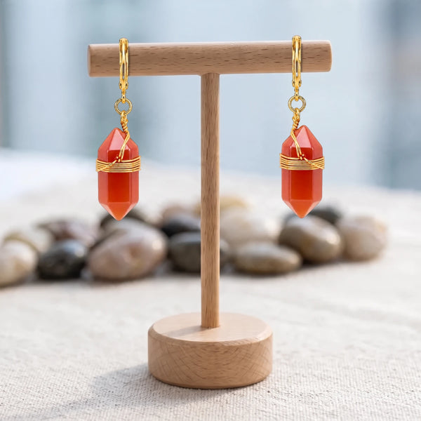 Boucles d'oreilles pierre orange, pointe de cornaline cerclée de fil doré, créoles sur un présentoir en bois