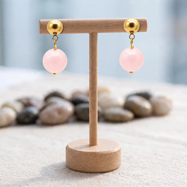Boucles d'oreilles pierre rose, boule de quartz rose 12 mm sous puce dorée, présentées sur un support en bois