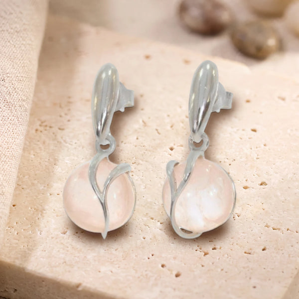 Boucles d'oreilles boule de quartz rose en argent 925 rhodié, paire posée sur une dalle de travertin