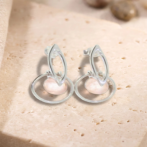 Boucles d'oreilles boule de quartz rose dans un cercle en argent 925 rhodié, paire posée sur une dalle de travertin