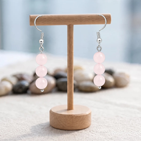 Boucles d'oreilles pierre rose, trois boules de quartz rose de 6 mm sur crochet acier argenté, sur un support en bois