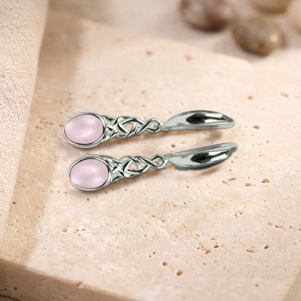 Boucles d'oreilles en quartz rose ovale à motif celtique en argent 925, paire posée sur une dalle de travertin