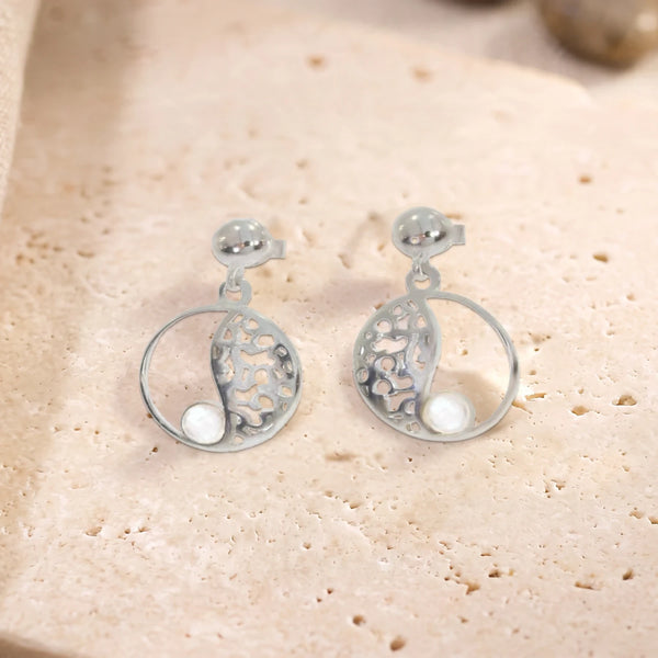 Boucles d'oreilles en quartz rose sur cercle ajouré en argent 925 rhodié, paire posée à plat sur une dalle de travertin