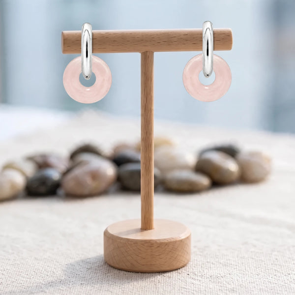 Boucles d'oreilles pierre rose, donut de quartz rose 15 mm sur créole argentée, présentées sur un support en bois