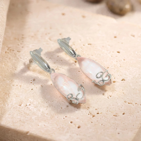 Boucles d'oreilles en quartz rose cabochon navette sur argent 925 rhodié, paire posée sur une dalle de travertin