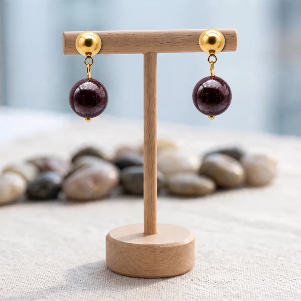 Boucles d'oreilles pierre rouge, boule de grenat 12 mm sur puce acier doré, présentées sur un support en bois