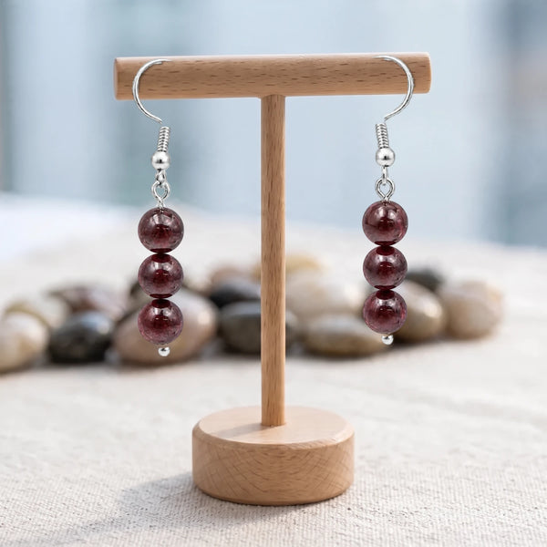 Boucles d'oreilles pierre rouge, trois boules de grenat sur crochet acier argenté, présentées sur un support en bois