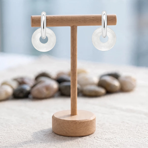 Boucles d'oreilles pierre transparente, donut de cristal de roche 15 mm sur créole argentée, sur un support en bois