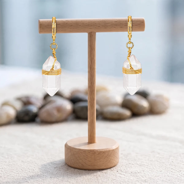 Boucles d'oreilles pierre transparente, pointe de cristal de roche et fil doré, créoles sur un présentoir en bois