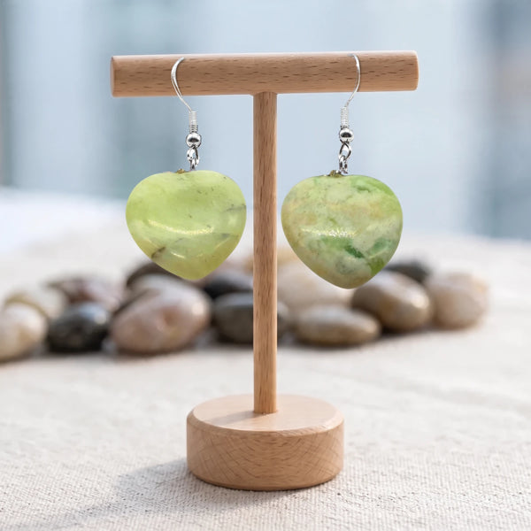 Boucles d'oreilles pierre verte, cœur en jade naturel pendant sur crochet argenté, présentées sur un support en bois