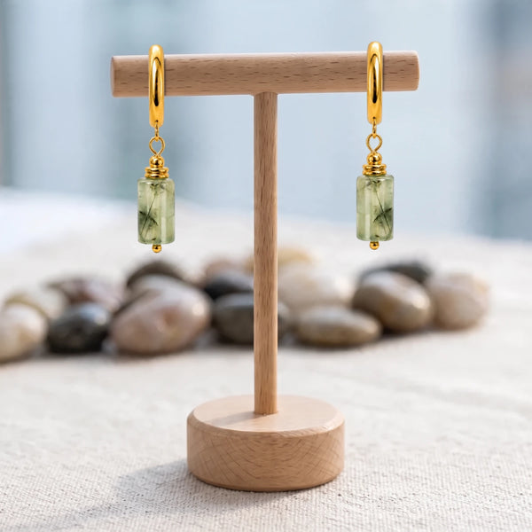 Boucles d'oreilles pierre verte, tube de préhnite sur créole acier doré, présentées sur un support en bois